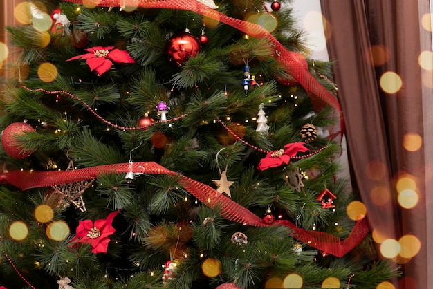공과 장난감, 보케가 있는 포인세티아 꽃으로 축제처럼 장식된 크리스마스 트리를 닫습니다.