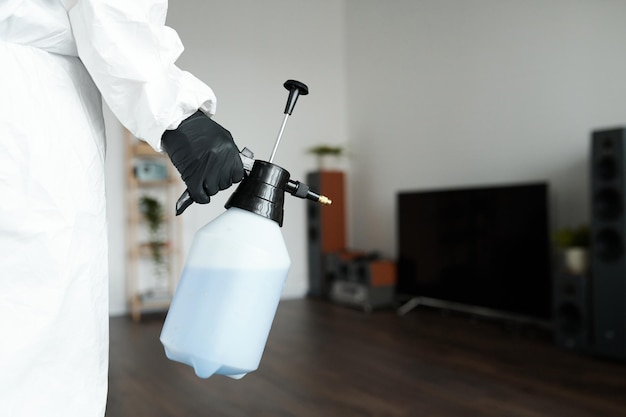 Близкий снимок уборщицы в защитном костюме, использующей опрыскиватель с моющим средством при выполнении домашней работы