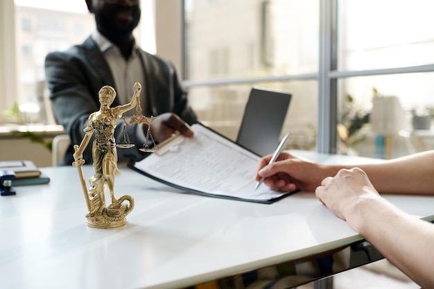 Closeup of client signing contract at meeting with lawyer in office