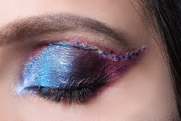 Closeup of closed eye with bright shiny shadows makeup lessons concept