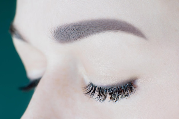 Closeup of closed eyes with artificial eyelashes black eyeliner ideal skin eyebrows of unrecognizable young woman