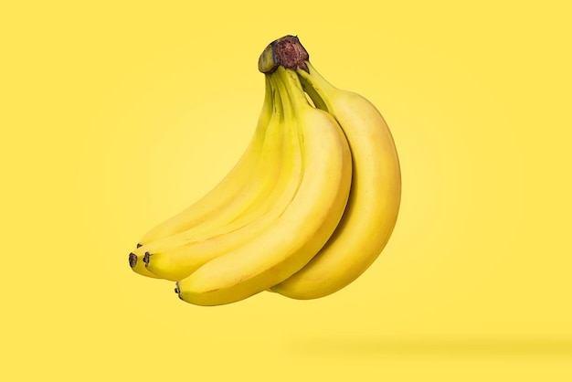 Closeup of a cluster of fresh isolated bananas suspended in the air on yellow background