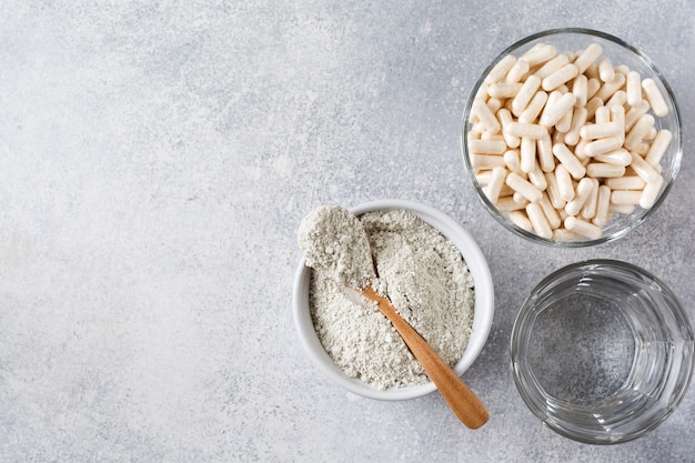 Closeup collagen for preparing a cosmetic mask in ceramic bowl with spoon and capsules for diet food, loofah sponges and dry eucalyptus branches on old gray concrete table. Flat lay