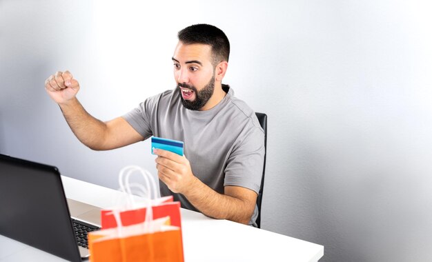 Closeup of colorful bags and background man excited about computer and holding card for online shopping concept shopping black friday cyber monday sales christmas