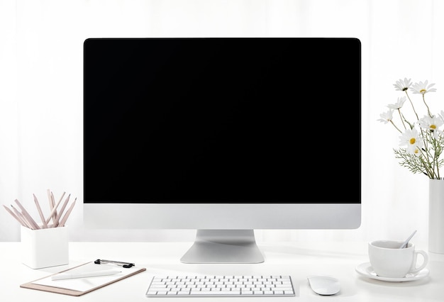 Closeup of a computer, a cup of coffee, a vase of flowers, and more on a white desk, indoors