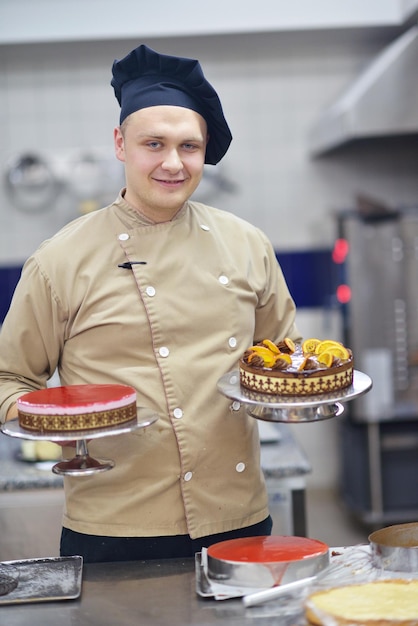 Closeup of a concentrated male pastry chef decorating dessert cake food in the kitchen