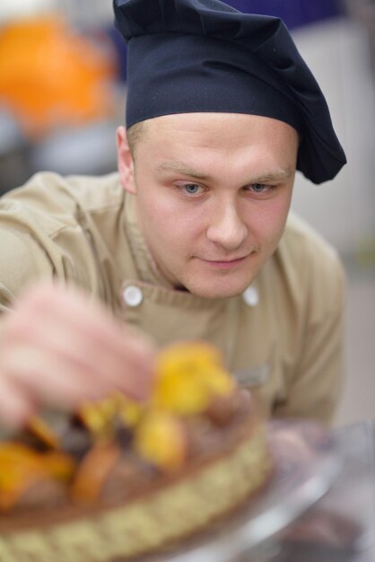 Closeup of a concentrated male pastry chef decorating dessert cake food in the kitchen