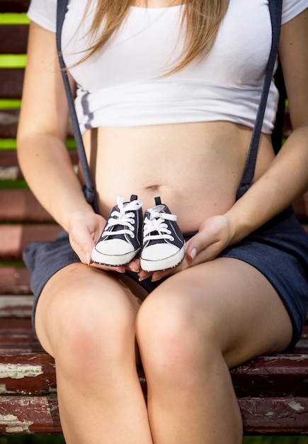 Closeup conceptual pregnant woman holding baby shoes on hands