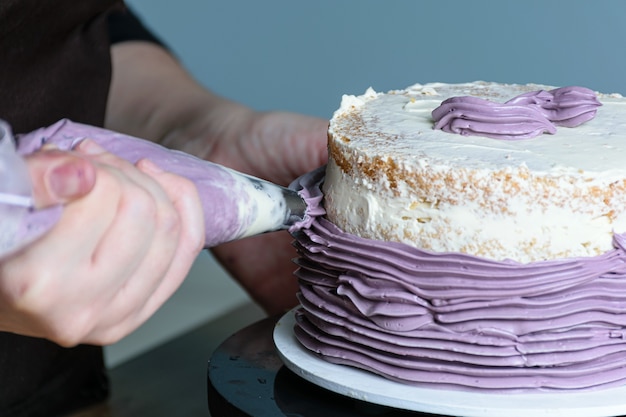 Closeup of confectioner's hand putting butter cream with icing spout, cake on turntable.