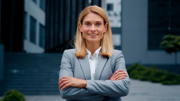 Closeup confident successful businesswoman in suit posing with crossed arms outdoors smiling woman