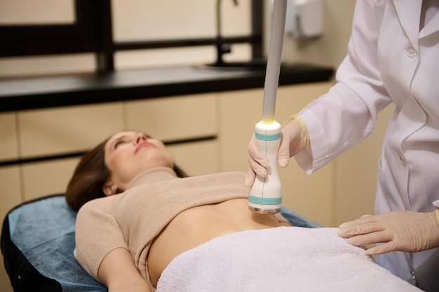 Closeup contact ultrasound sensor in the hand of a beautician giving cavitation body contouring anticellulite slimming treatment in wellness spa