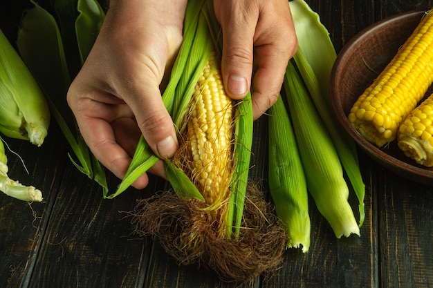 Closeup of a cook hands while peeling ripe corn cob Cooking maize on the kitchen table with the hands of a cook