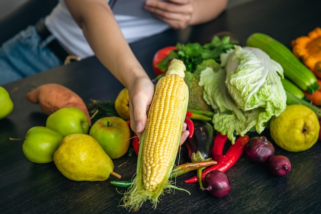 Closeup corn in female hands and other vegetables on the kitchen table