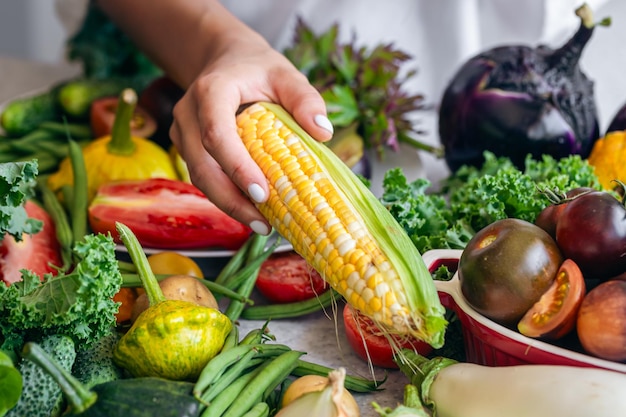 Closeup corn in female hands and other vegetables on the kitchen table