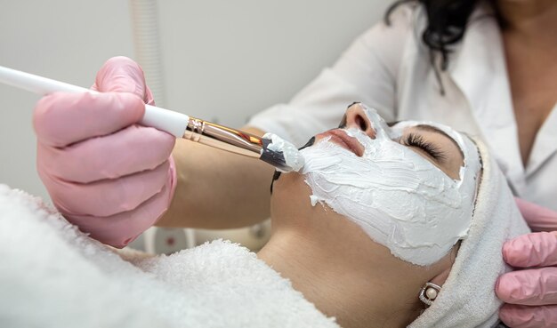 Closeup of cosmetologist applying white cosmetic facial mask for her female patient at spa salon