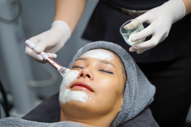 Closeup cosmetologist use cosmetic brush applying facial jelly's gel on woman client face