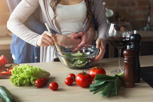 自宅のロフトキッチンで一緒に健康的な料理を調理するカップルのクローズアップ。野菜サラダの準備。
