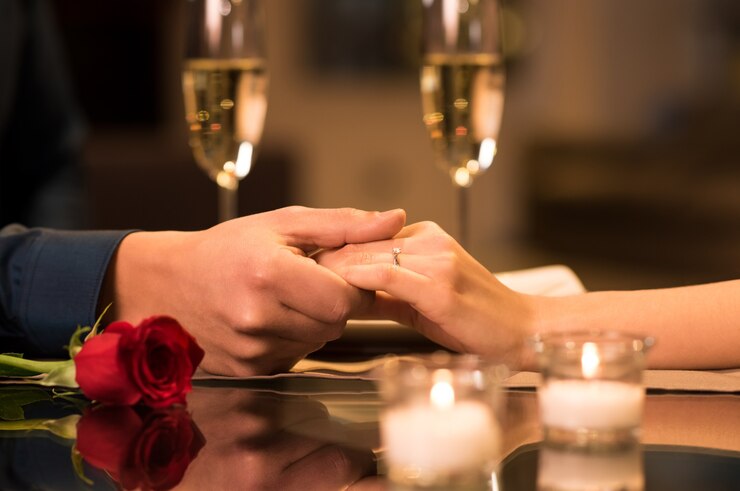 Photo closeup of couple hands on restaurant table with two glasses of champagne in background.