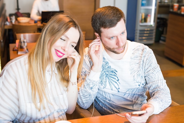 Closeup of couple listening to music with mobile phone at coffee bar. Man and woman listening music with headphones.