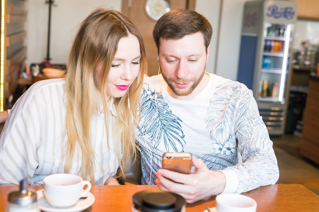 Closeup of couple listening to music with mobile phone at coffee bar. Man and woman listening music with headphones.