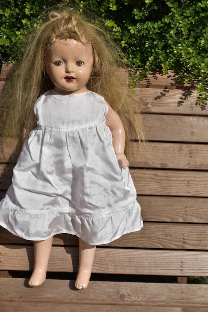 Photo closeup of creepy old doll standing on a wooden bench