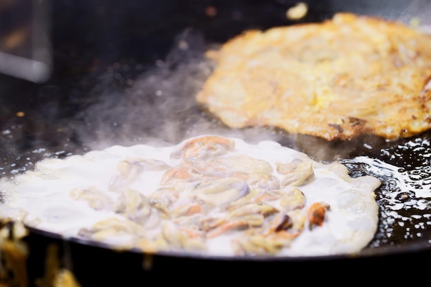 Primo piano di frittelle di cozze fritte croccanti o frittata di cozze sul mercato di cibo di strada tailandese in padella calda