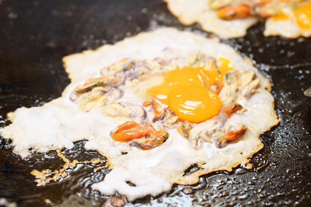 Foto primo piano di frittelle di cozze fritte croccanti o frittata di cozze sul mercato di cibo di strada tailandese in padella calda