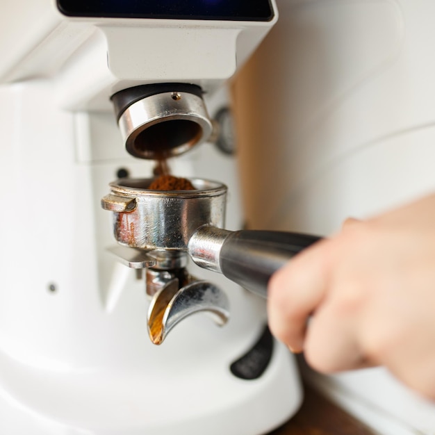 Крупный план урожая бариста с молотым кофе в портафильтре, готовящего вкусный горячий напиток в кафе