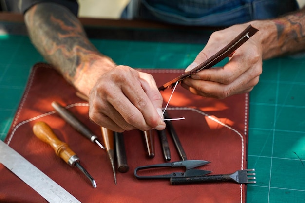 closeup and crop hands of leather craftsman sewing a leather brown bag for a customer