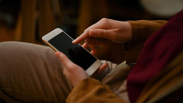 Closeup cropped image Female relaxes sitting on comfy chair and using her modern smartphone