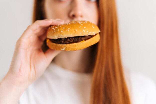 クローズアップは、食欲をそそるおいしいハンバーガーのかみ傷を喜ばせる認識できない若い女性のショットの顔をトリミングしました