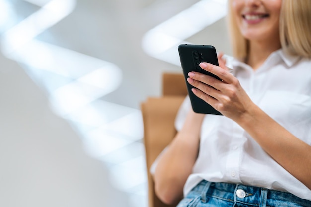 Closeup cropped shot of unrecognizable cheerful blonde young woman using mobile phone holding