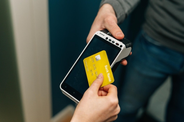 Closeup cropped shot of unrecognizable courier male giving POS wireless terminal to making contactless payment via credit card to young female customer