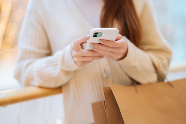 Closeup cropped shot of unrecognizable young woman using typing smartphone holding shopping bags