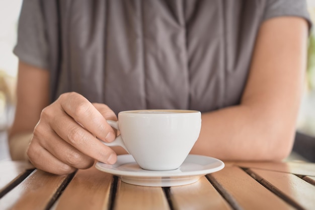 Closeup of a cup of cappuccino or hot drink and the hands of a young woman drinking coffee during a break Selective focus on fingers idea for background