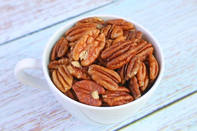 Closeup a Cup Filled with Pecan Nuts on Pale Blue Wooden Table