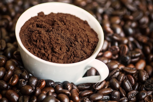 closeup of a cup of ground coffee on the heap of roasted coffee beans shot in the studio