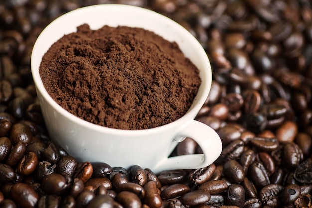 Closeup of a cup of ground coffee on the heap of roasted coffee beans shot in the studio