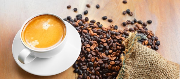 Closeup of a cup of latte with golden foam and blend coffee beans in a brown sack on an old wooden