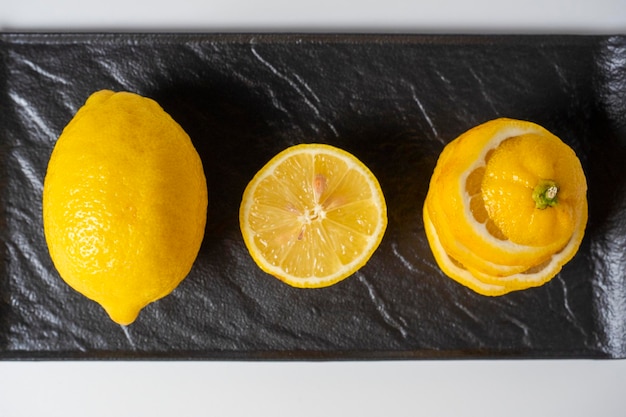 A closeup of a cut and whole lemon lies on a black textured plate White background Top view flat lay A healthy citrus fruit full of vitamins