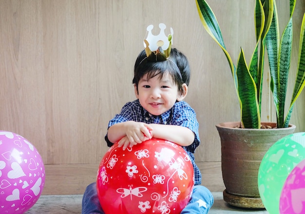 Closeup cute asian kid with paper crown and balloon in birthday party in room textured background with copy space