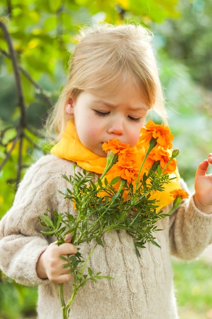 Photo closeup cute little girl in yellow scarf with closed eyes sniffing fragrant orange flowers outdoors