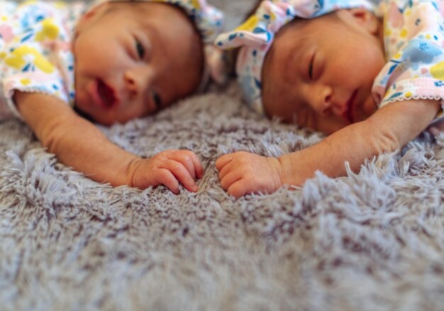 Photo closeup of cute newborn twin baby girls laying on a gray blanket and holding hands