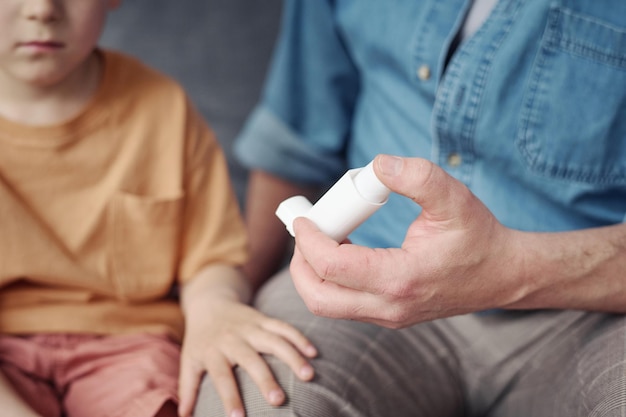 Closeup of dad giving inhaler to his little son with asthma during the attack