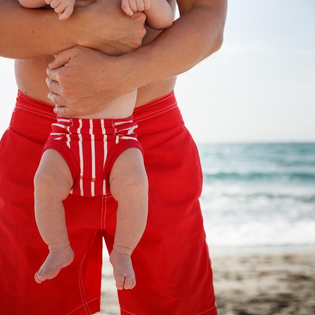 Closeup of a dad hugging his newborn son against the background\
of the ocean shore outdoors