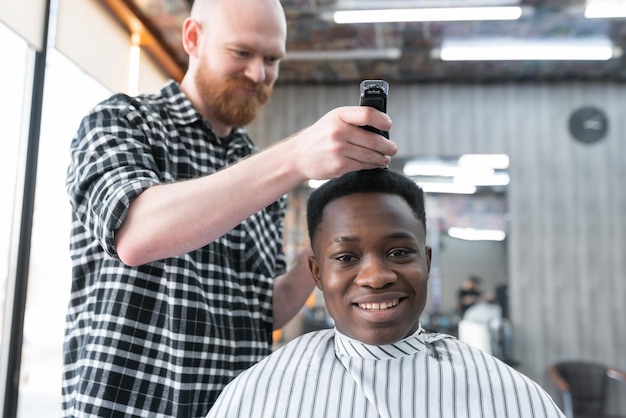 Primo piano uomo dalla carnagione scura cliente in un barbiere un parrucchiere con un clipper nelle sue mani taglia i capelli di un giovane barbershop concept