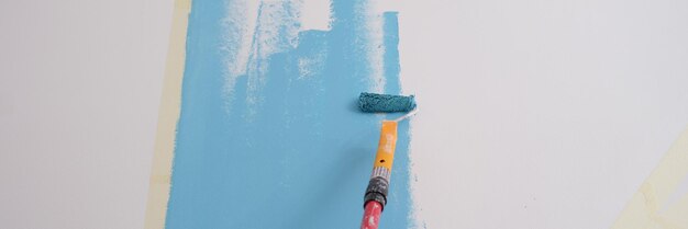 Closeup of decorator painting walls in light blue color with roller interior decorating or