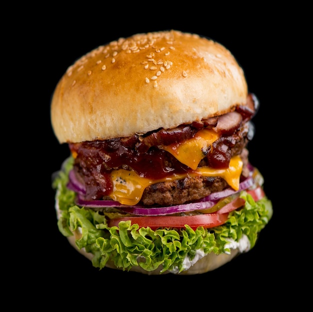 Closeup of a delicious fresh homemade burger with lettuce cheese onion and tomato on a rustic wooden board on a dark background