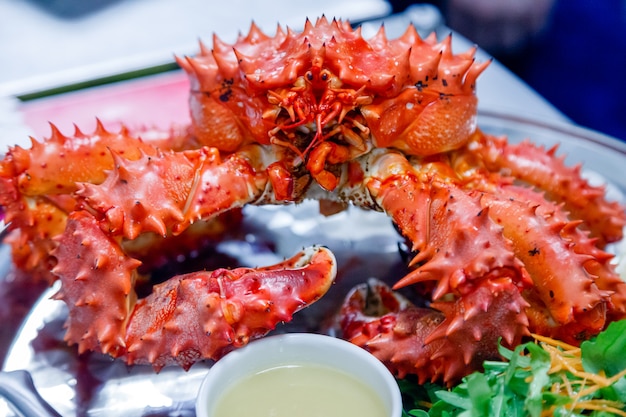 Closeup of delicious tasty boiled freshly prepared red king crab on metal dish with lemon, greens, sauce. 