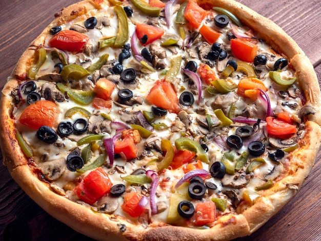 Closeup of a delicious vegetarian pizza with vegetables and mushrooms on a brown wooden background Unhealthy food Delicacy for vegetarians